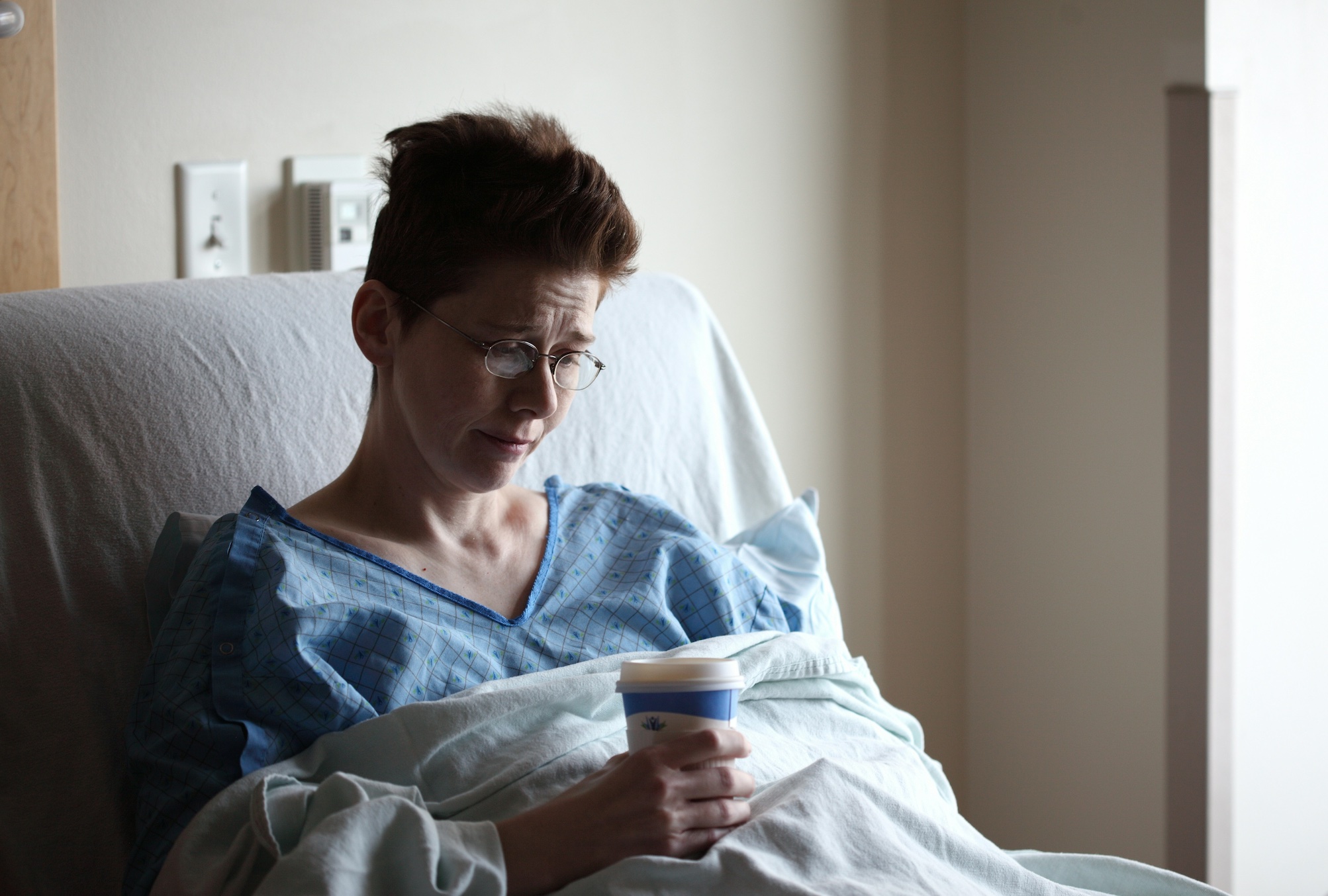 Woman in hospital bed with to go cup; image by Alexander Grey, via Unsplash.com.