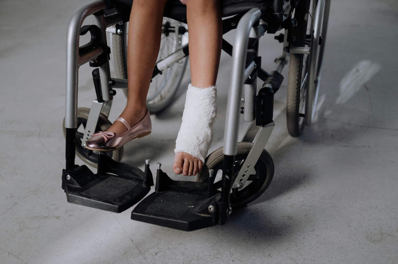 Girl with cast on foot and ankle sitting in wheelchair; image by cottonbro studio, via Pexels.com.
