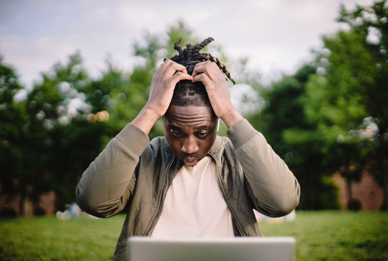 Stressed black male entrepreneur working on laptop in park; image by Ketut Subiyanto, via Pexels.com.