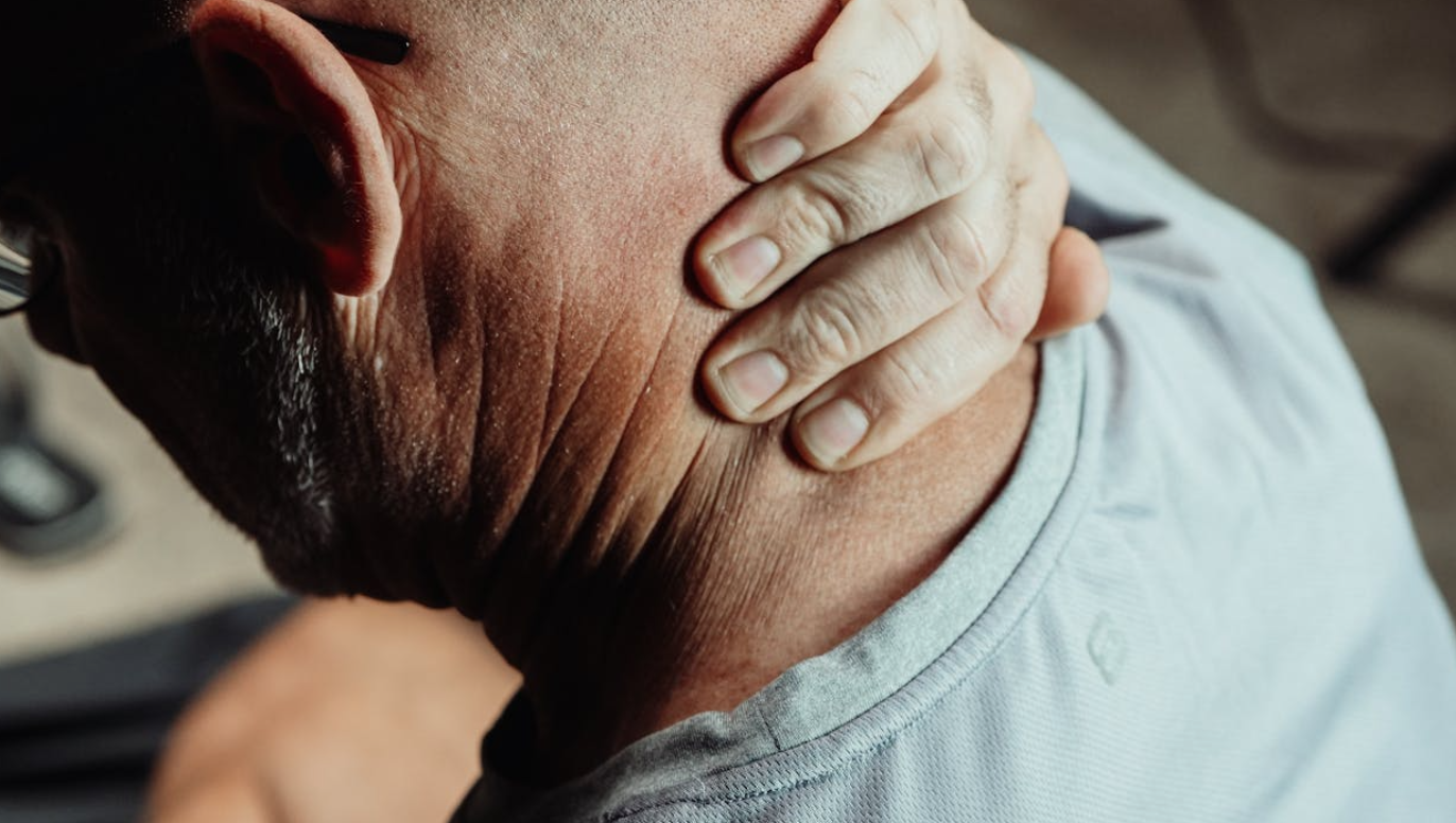 Close up of man with neck pain massaging his neck; image by Kindel Media, via Pexels.com.
