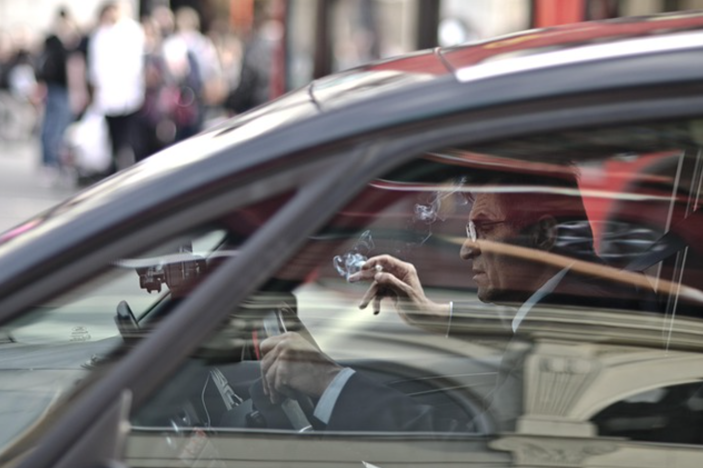 Man behind the wheel of a car smoking a cigarette; image by Whitechappel79, via Pixabay.com.