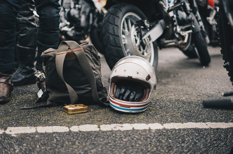 White helmet next to black backpack and parked motorcycle; image by Ambitious Studio*:Rick Barrett, via Unsplash.com.