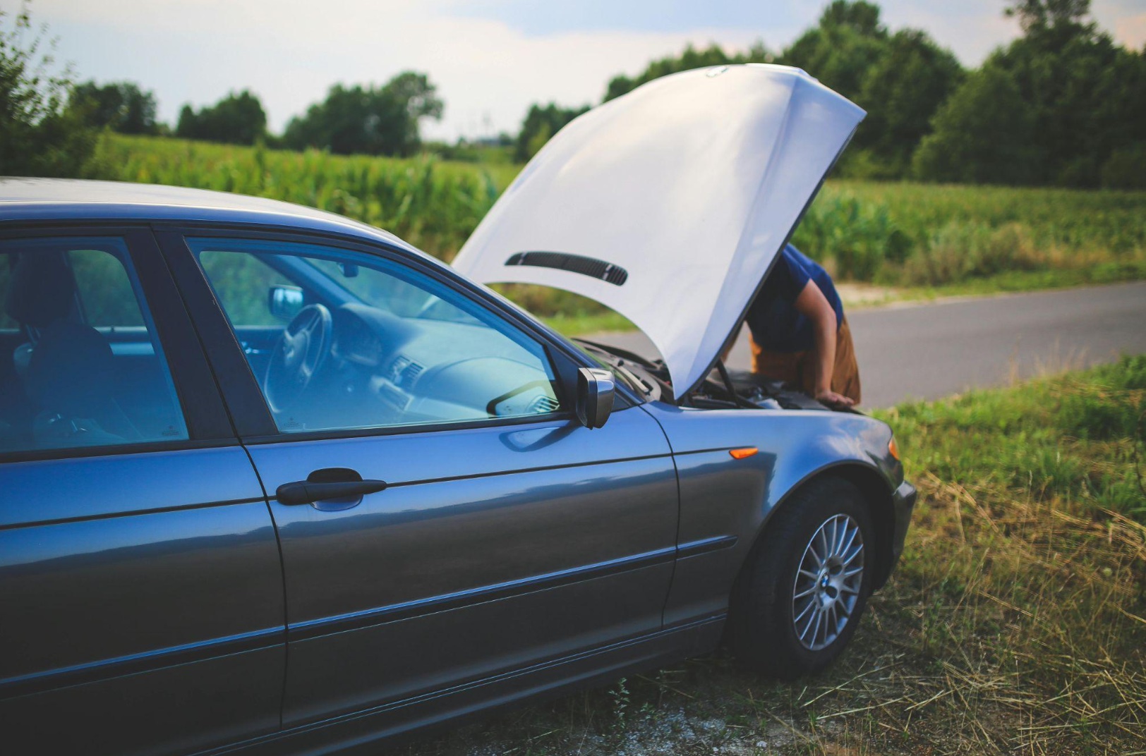Man looking under hood of car at side of road; image by karolinagrabowska, via Pixabay.com.