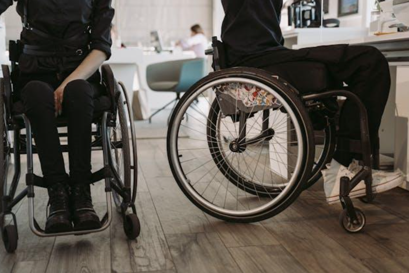 Two people wearing black sitting in wheelchairs; image by Mart Production, via Pexels.com.