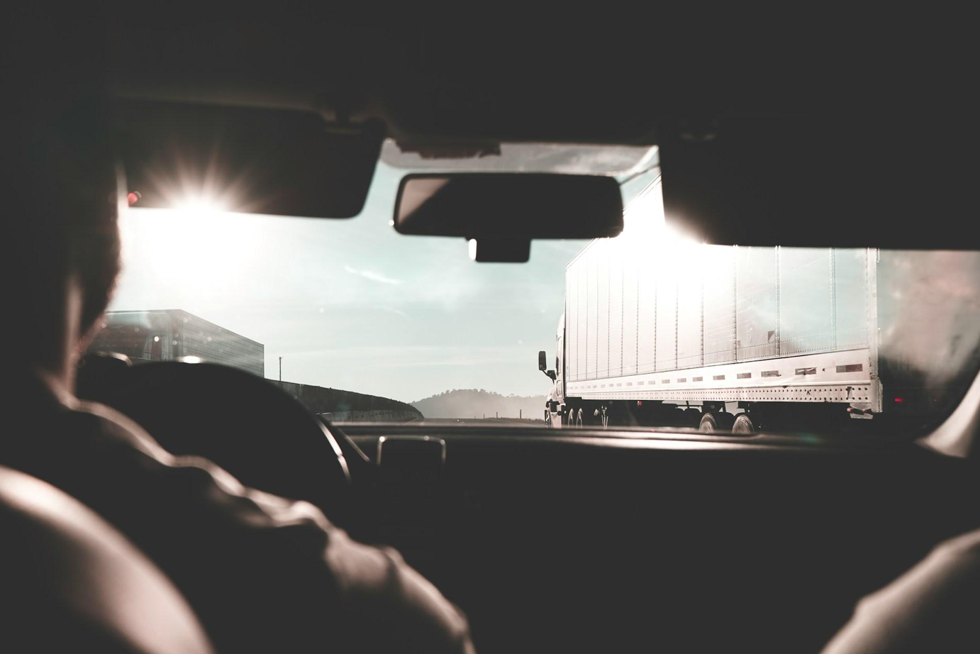 Man driving car with truck ahead and to his right; image by Eduardo Cano Photo Co., via Unsplash.com.