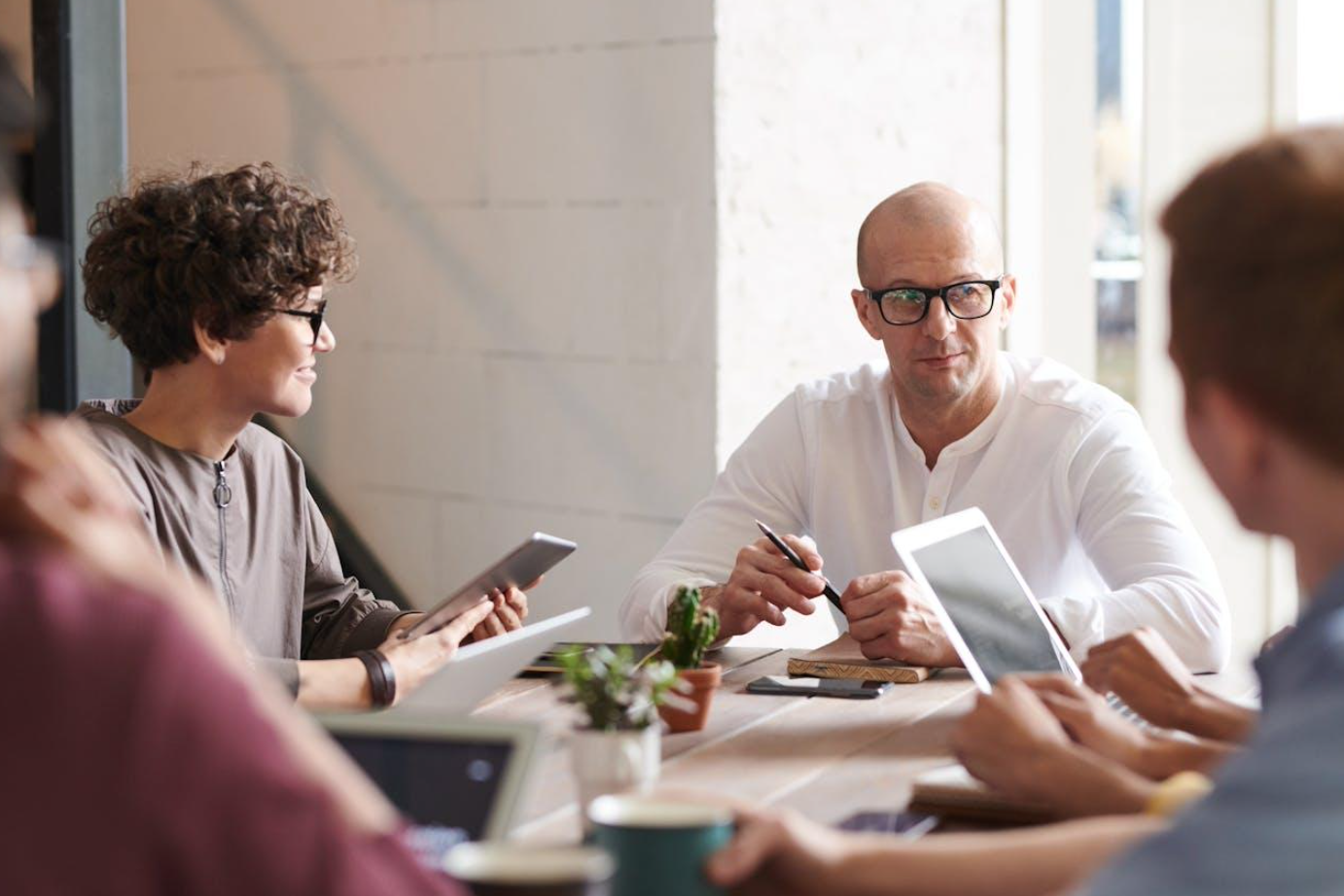 Man sitting at table with other people; image by fauxels, via Pexels.com.