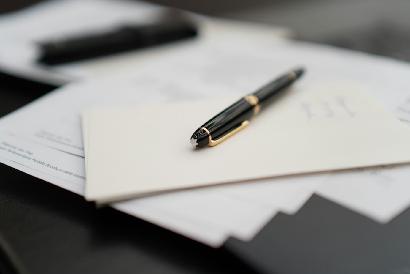 Pen sitting on top of a pile of papers; image by Andres Vera, via Unsplash.com.