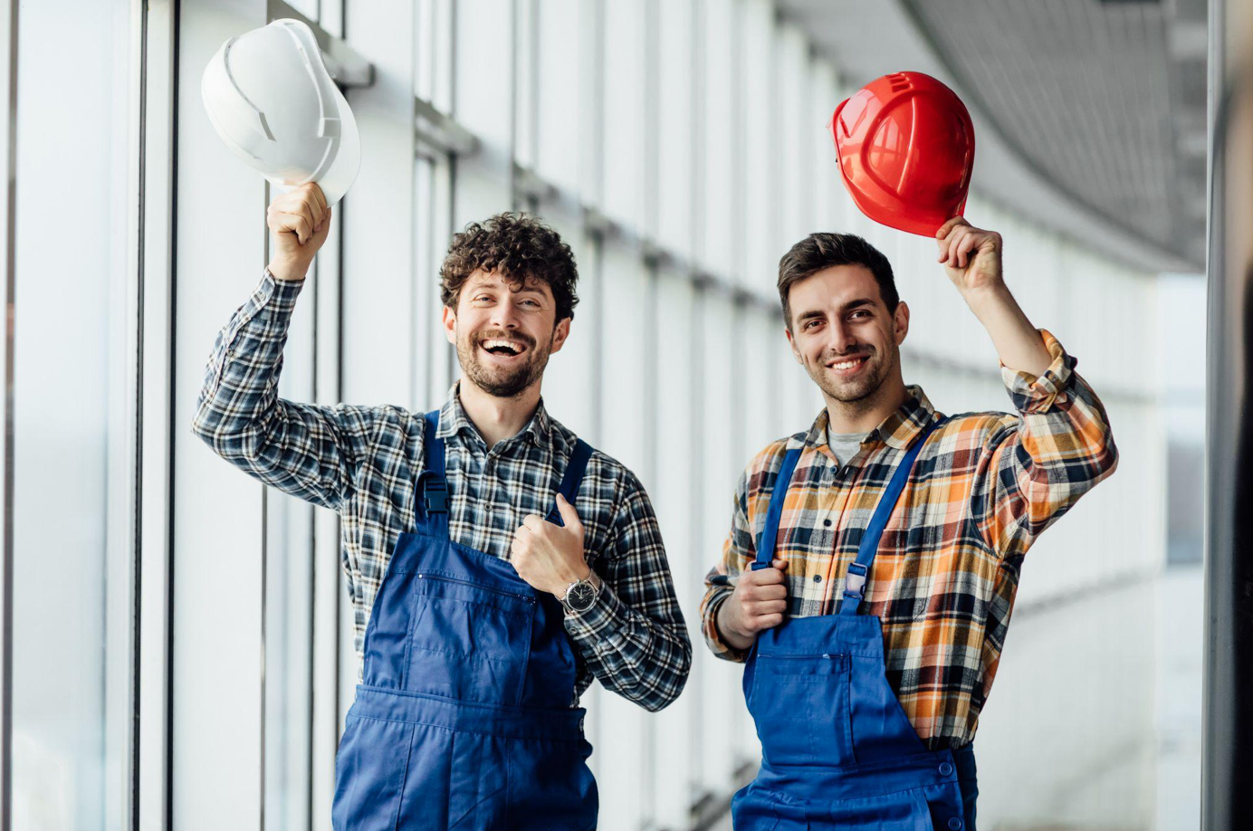 Two male construction workers smiling and doffing their helmets; image by artursafronovvvv, via Freepick.com.