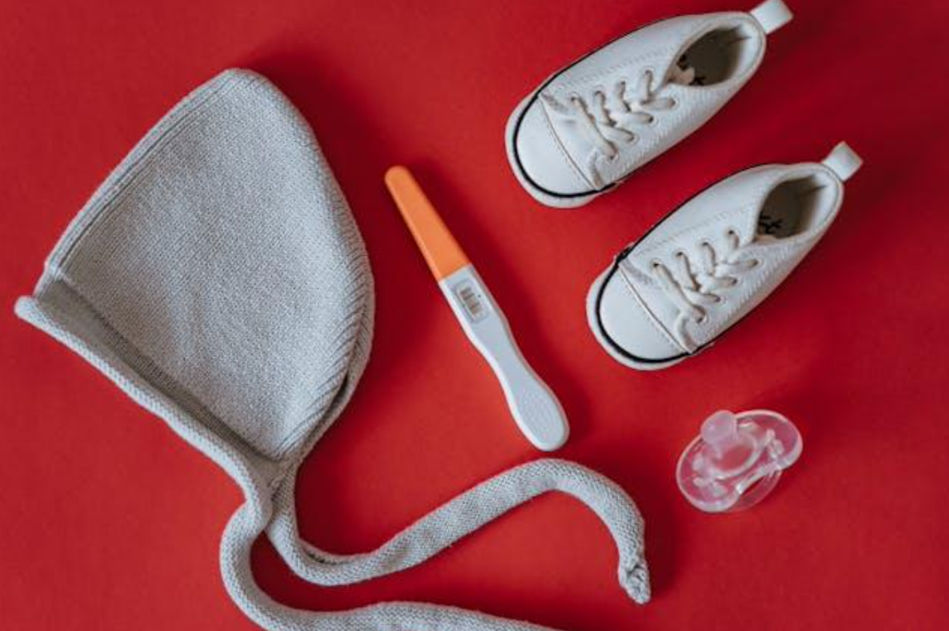 Closeup of pregnancy test near baby hat, shoes, and pacifier; image by olia danilevich, via Pexels.com.