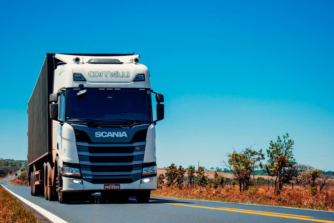 White semi-truck on road during the day; image by Gabriel Santos, via Unsplash.com.