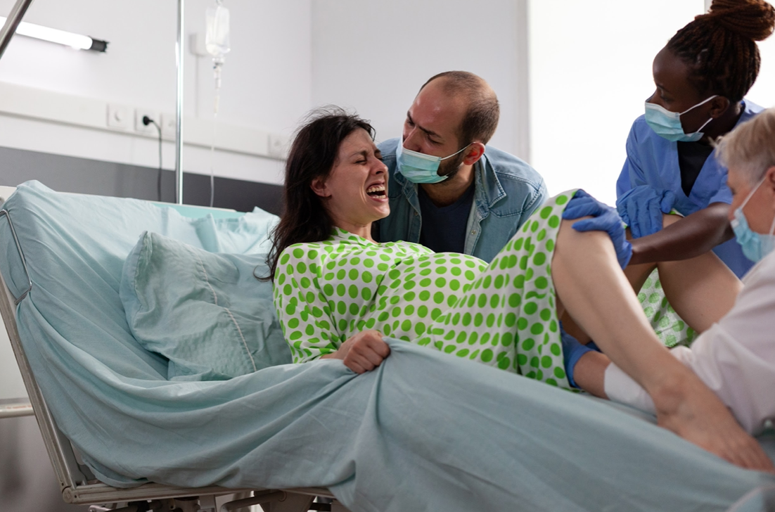 Woman having painful contractions during labor, medical team delivering baby; image by DC Studio, via Freepik.com.