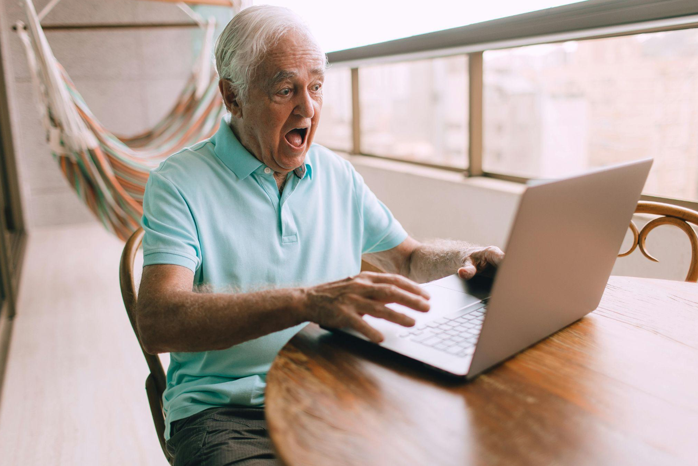Man sitting at table looking at laptop, appearring stunned; image by Helena Lopes, via Pexels.com.