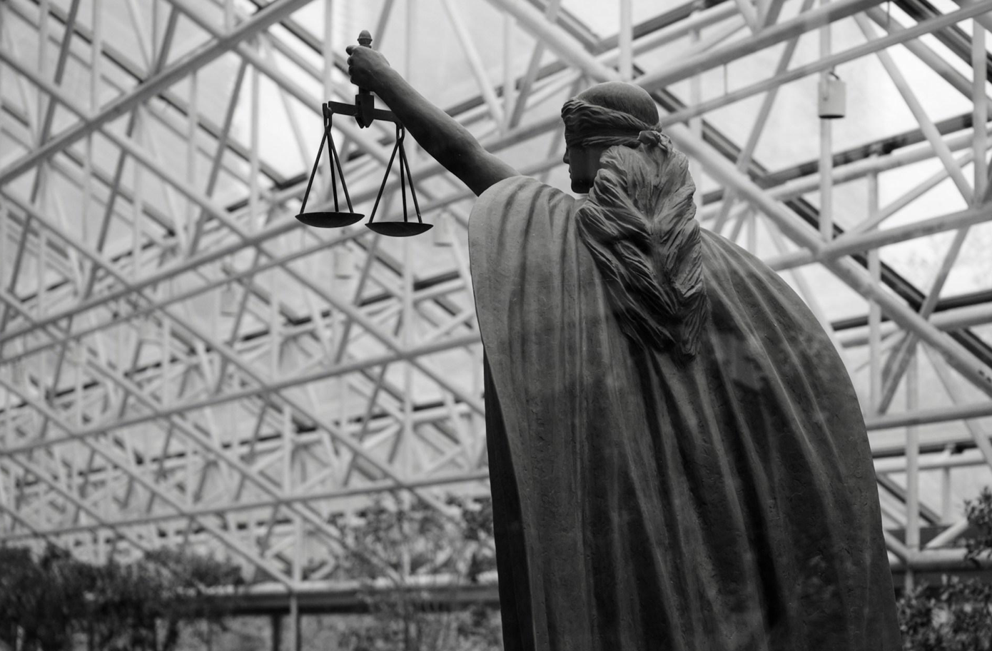Statue of lady justice holding scales; image by Albert Stoynov, via Unsplash.com.