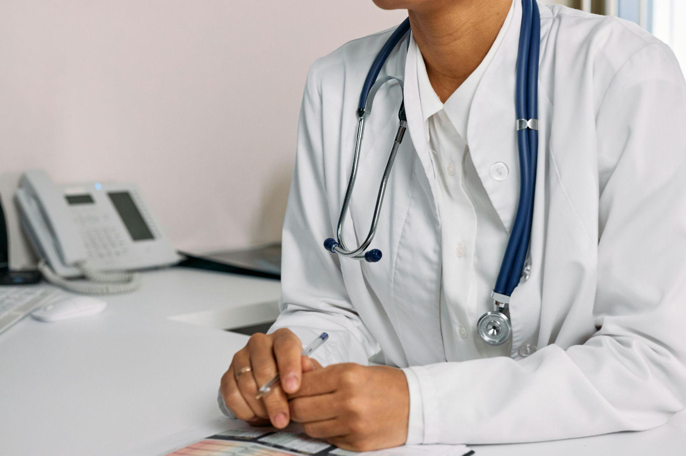 Woman in white coat sitting at a table; image by cottonbro studio, via Pexels.com.