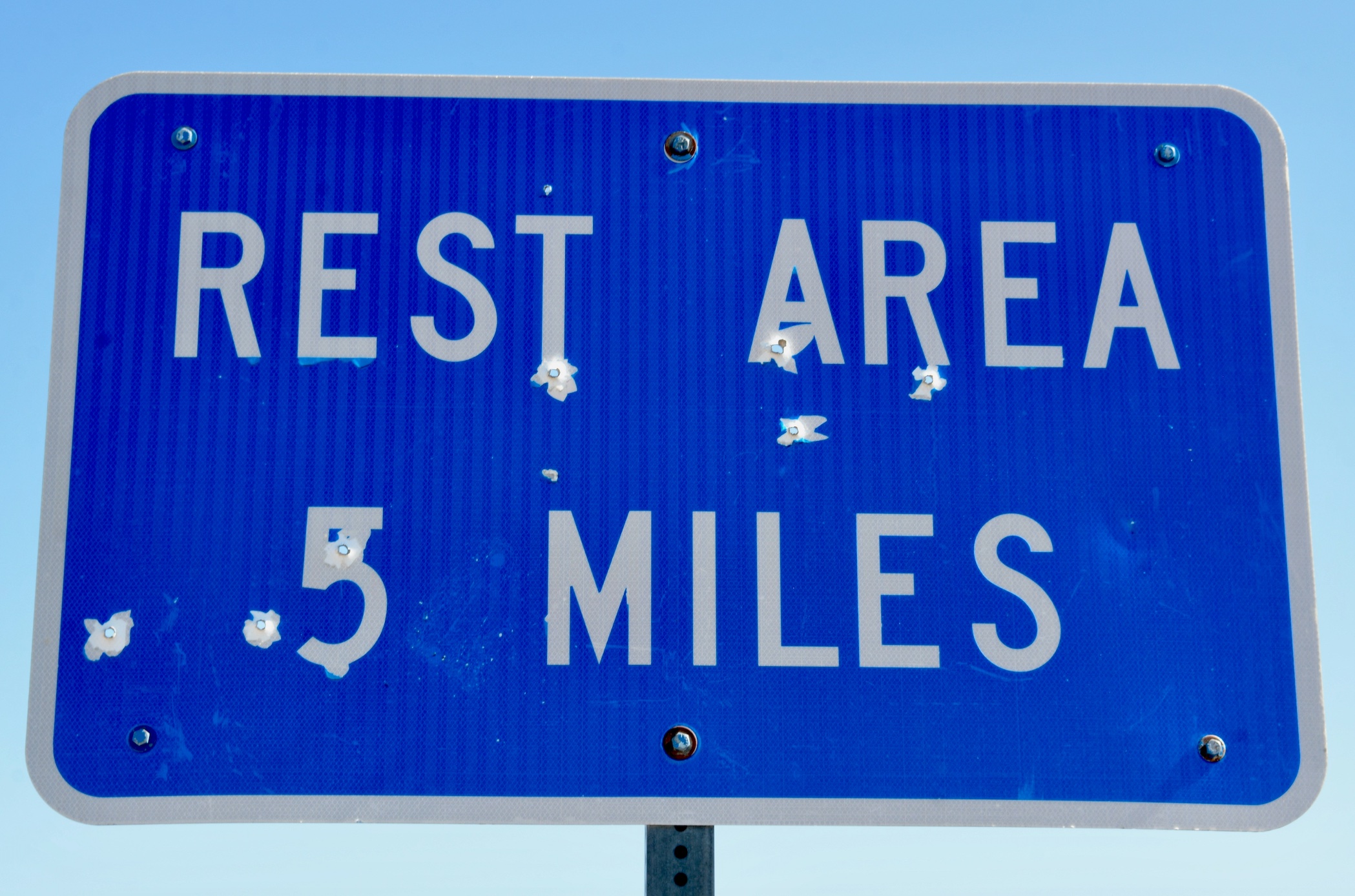 Blue sign with white lettering saying Rest Area 5 Miles; image by Joseph Two, via Unsplash.com.