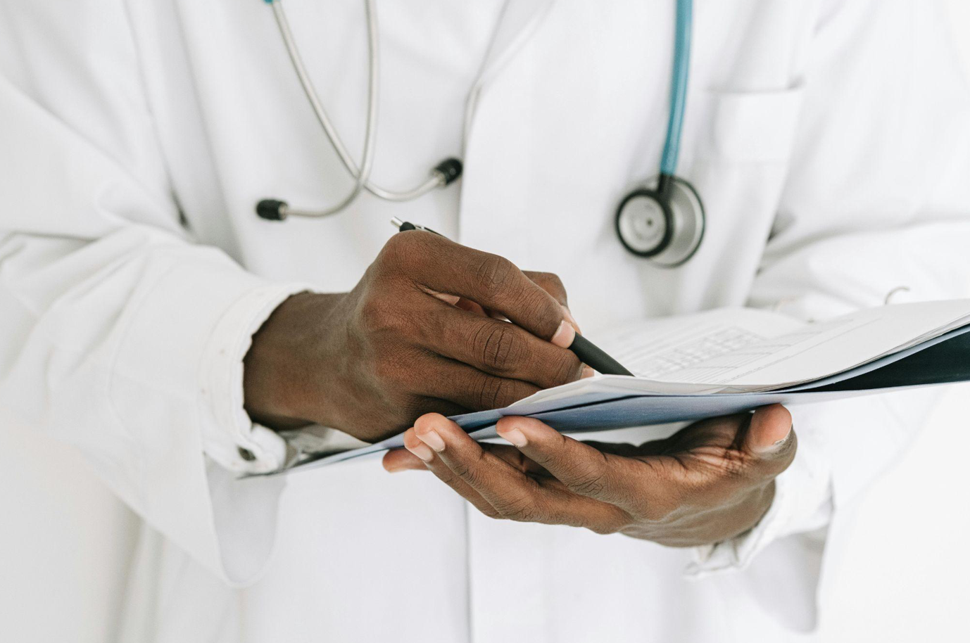 Doctor writing in chart; image by Ivan S, via Pexels.com.