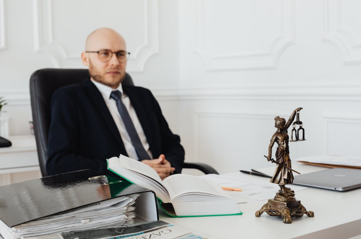 Bald man with glasses in black suit sitting at desk; image by www.kaboompics.com, via Pexels.com.