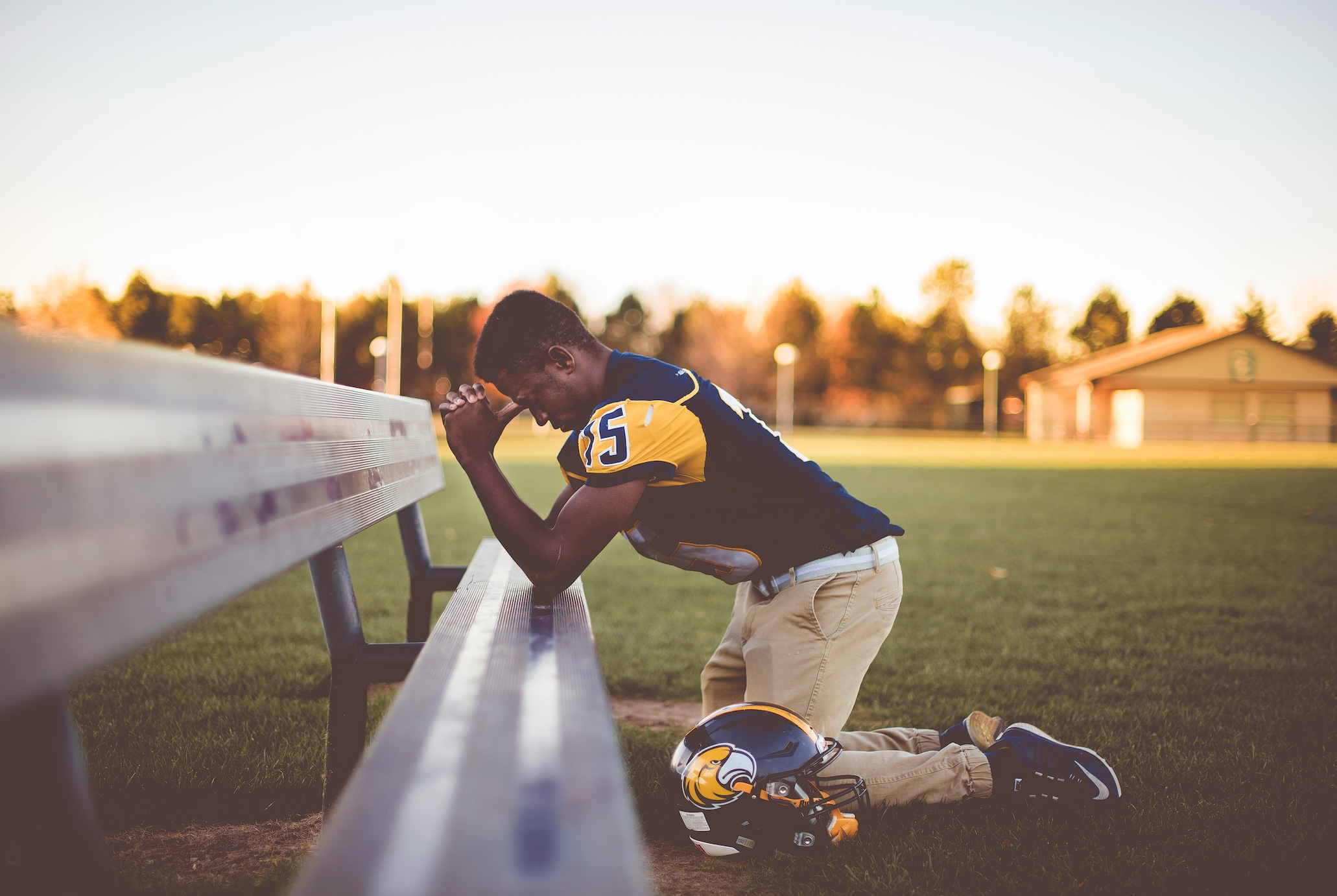 Football player kneeling on ground; image by Ben White, via Unsplashe.com.
