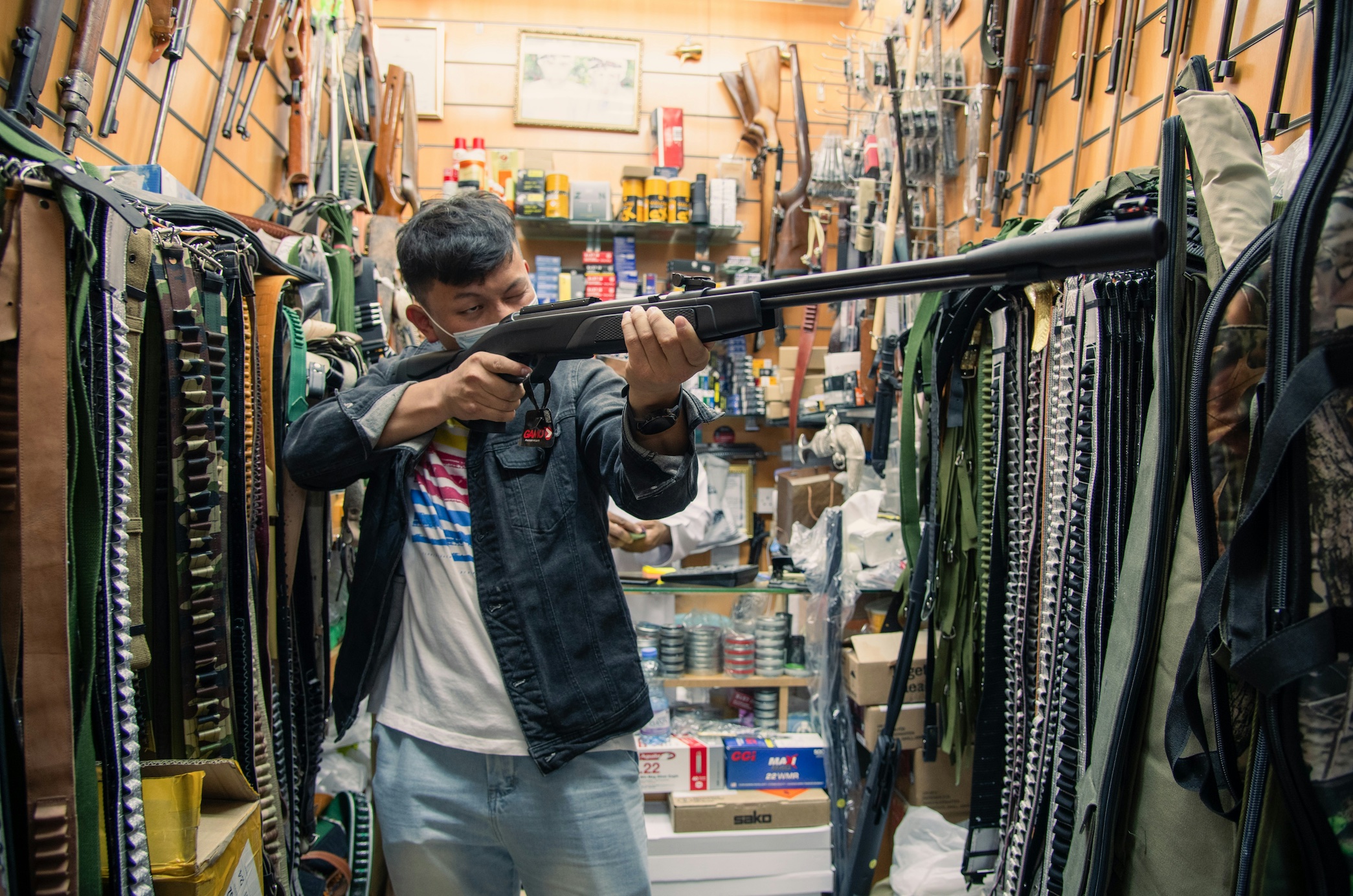 Man holding a rifle inside a store; image by Shuxin Wu, via Unsplash.com.