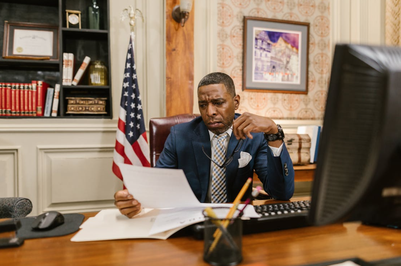 Man in blue suit at desk reading paperwork; image by RDNE Stock project, via Pexels.com.