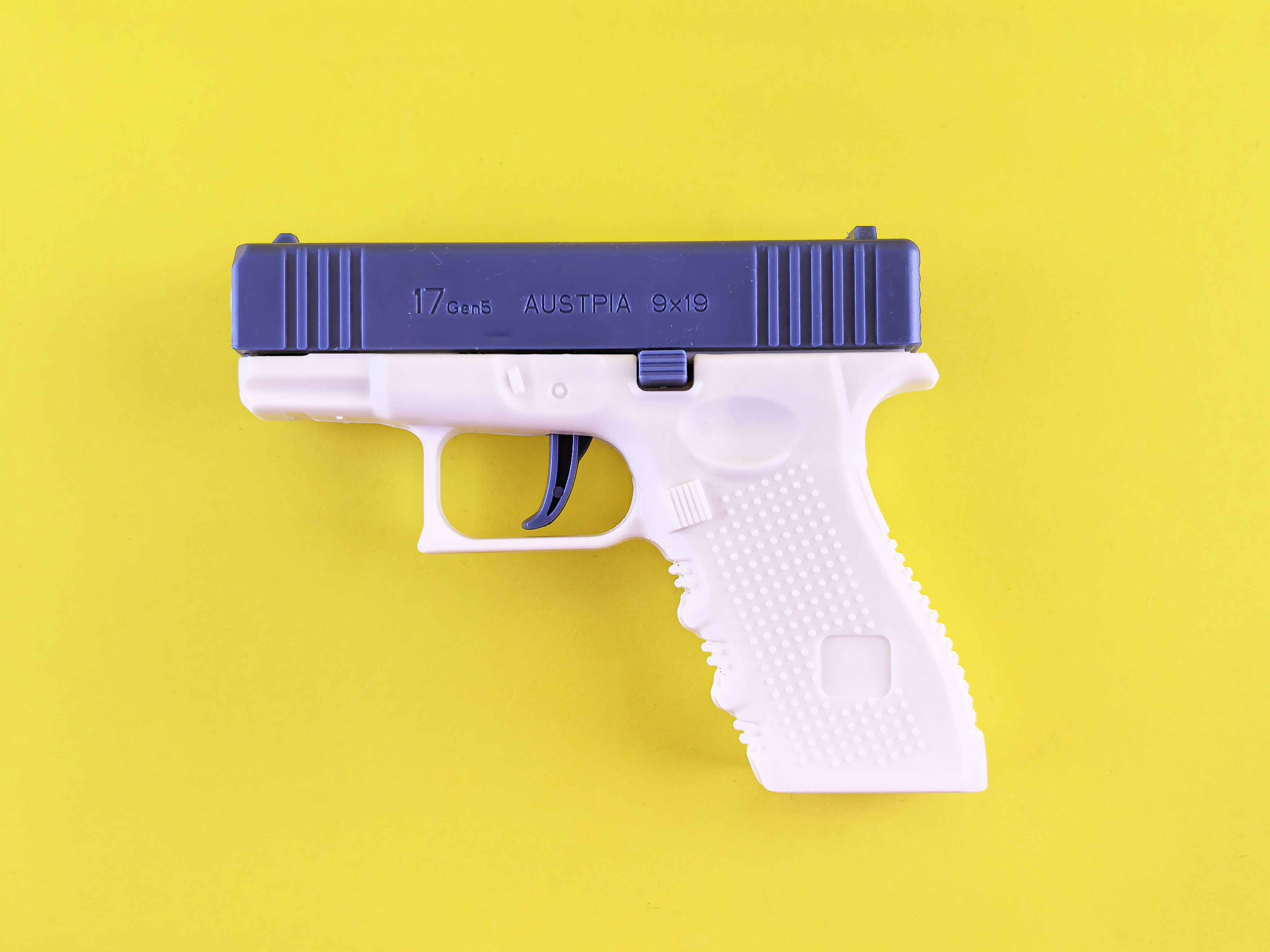 Plastic gun on a yellow background; image by Andrey Matveev, via Unsplash.com.