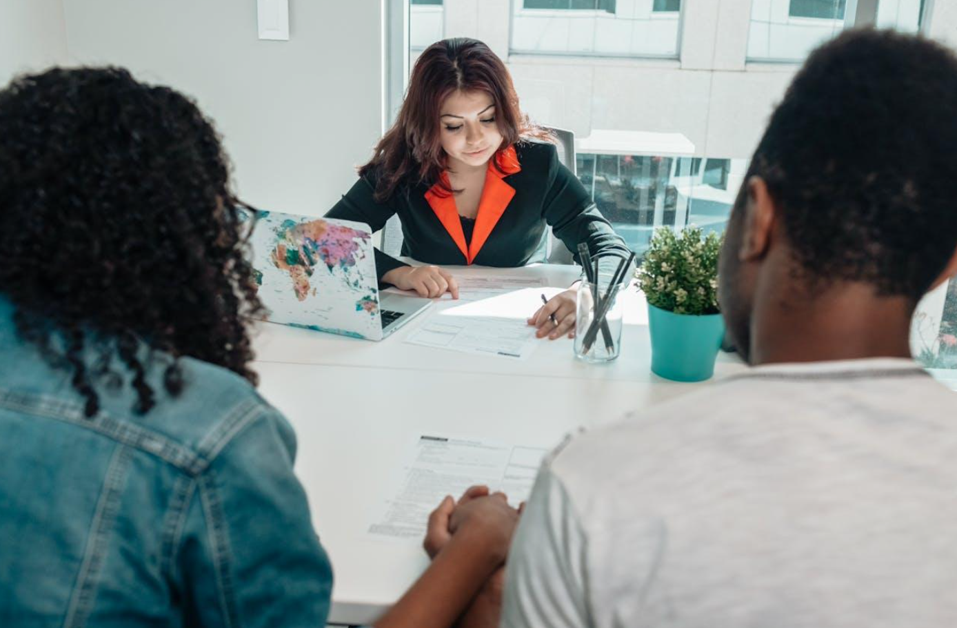 Couple holding hands while talking to woman across from them at a desk; image by Kindel Media, via Pexels.com.
