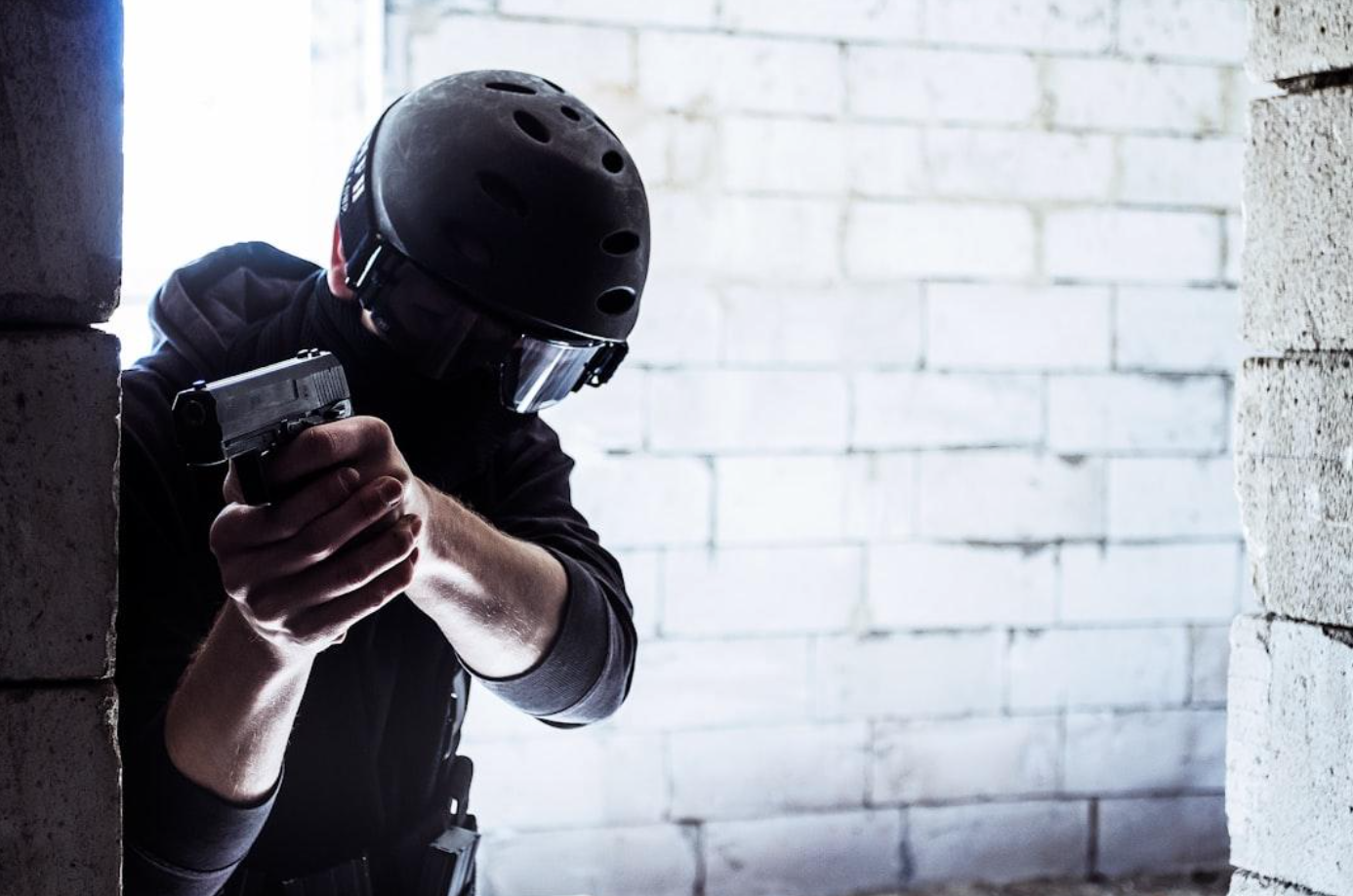 Man in black helmet aiming gun around a corner; image by Kevin Woblick, via Unsplash.com.