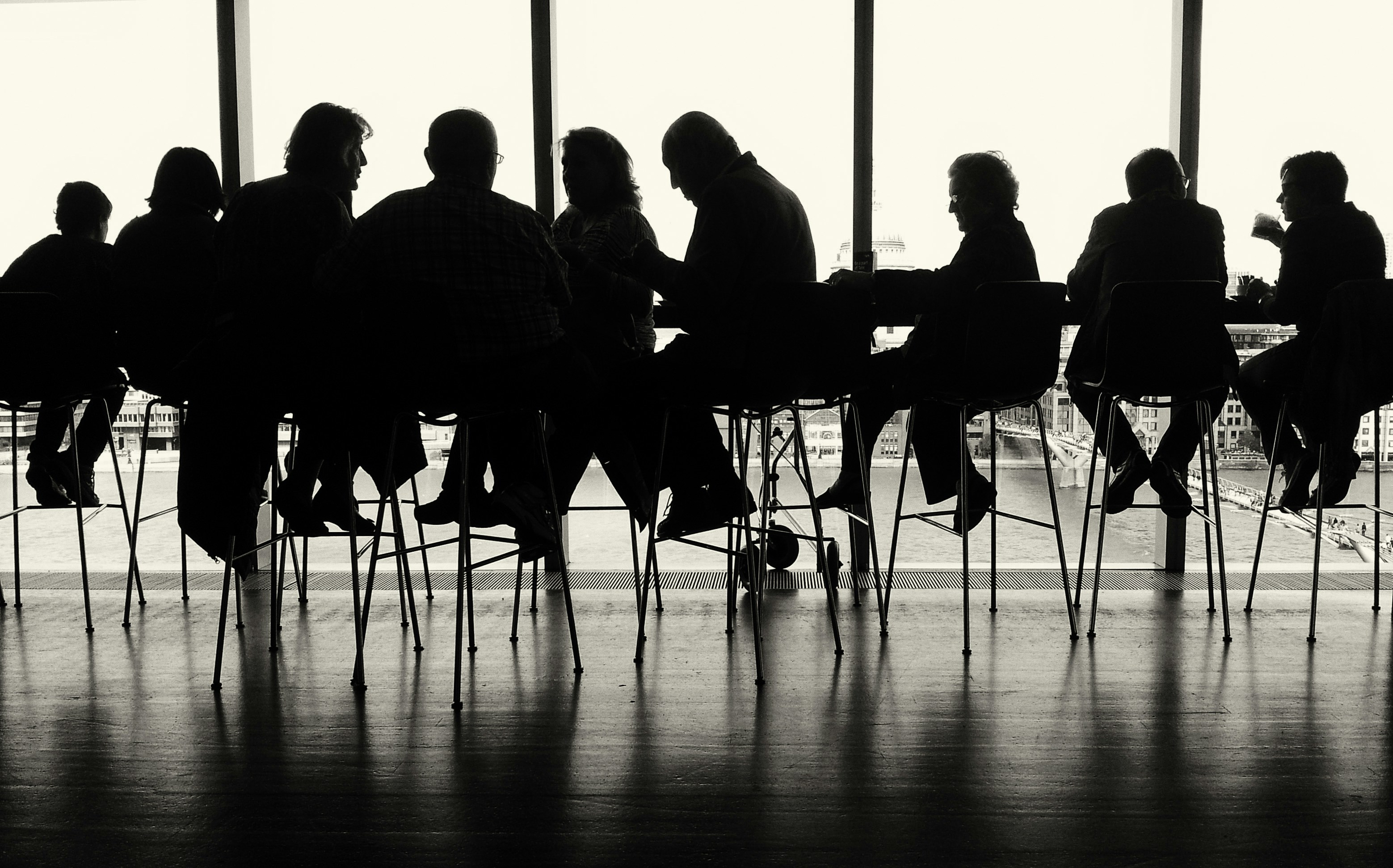 Silhouette of people sitting at a table in front of a window; image by Marco Bianchetti, via Unsplash.com.