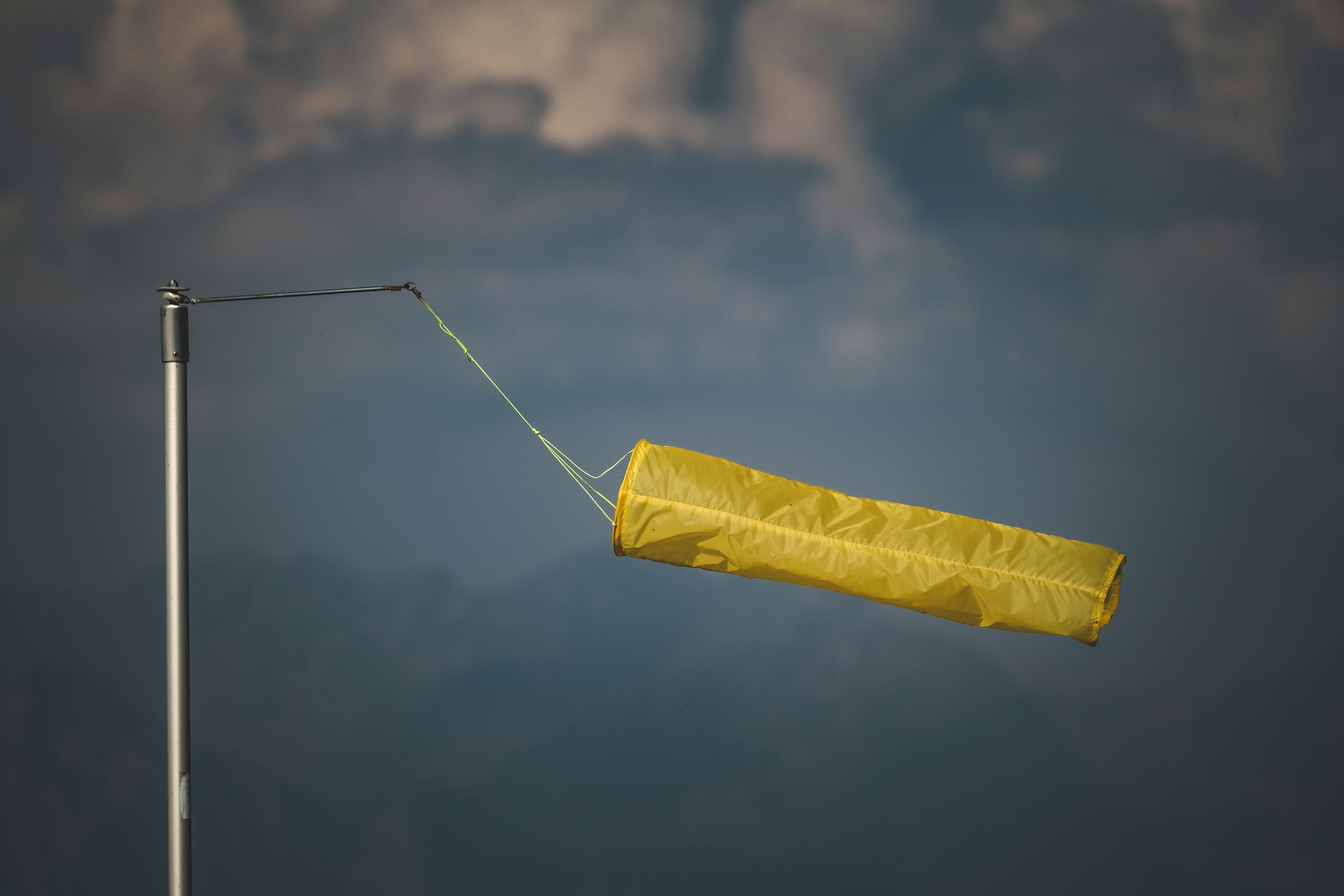 An isolated yellow windsock indicating wind direction against a dark, cloudy backdrop; image by Francesc Ungaro, via Pexels.com.
