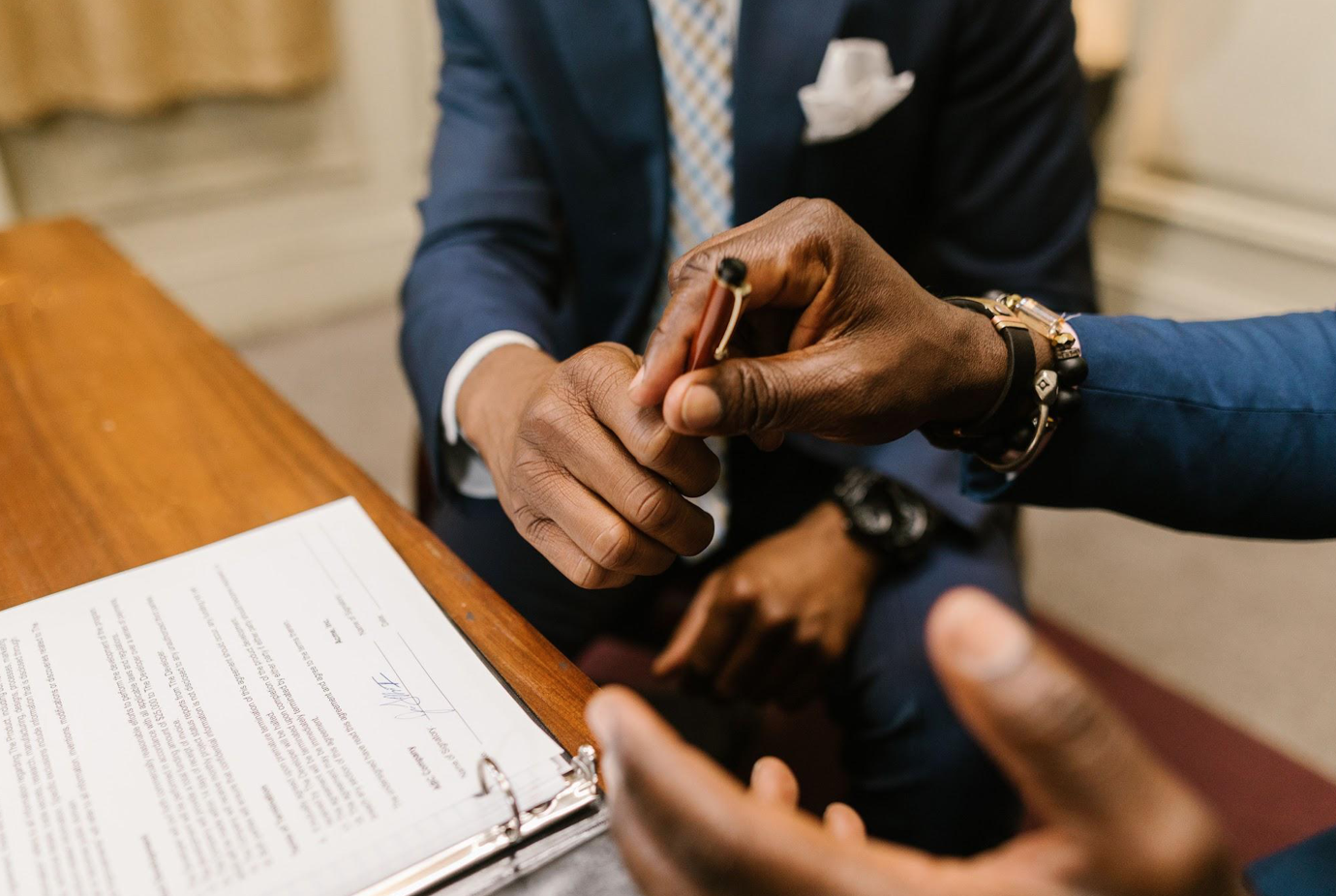 Closeup of one man giving a pen to another man to sign documents; image by RDNE Stock project, via Pexels.com.