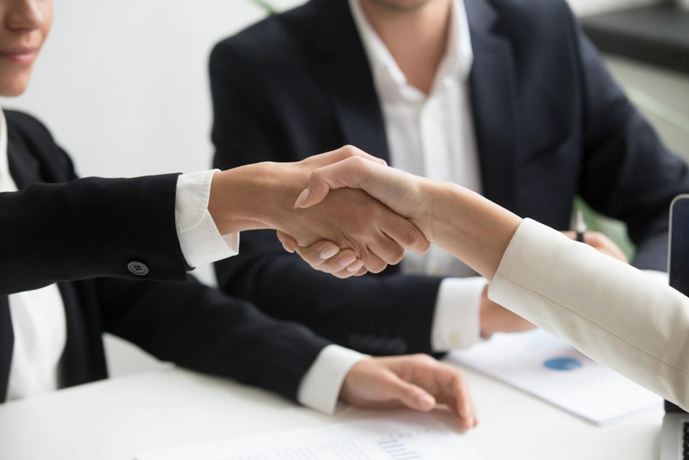Two people shaking hands at desk with laptop; image by Radission US, via Unsplash.com.