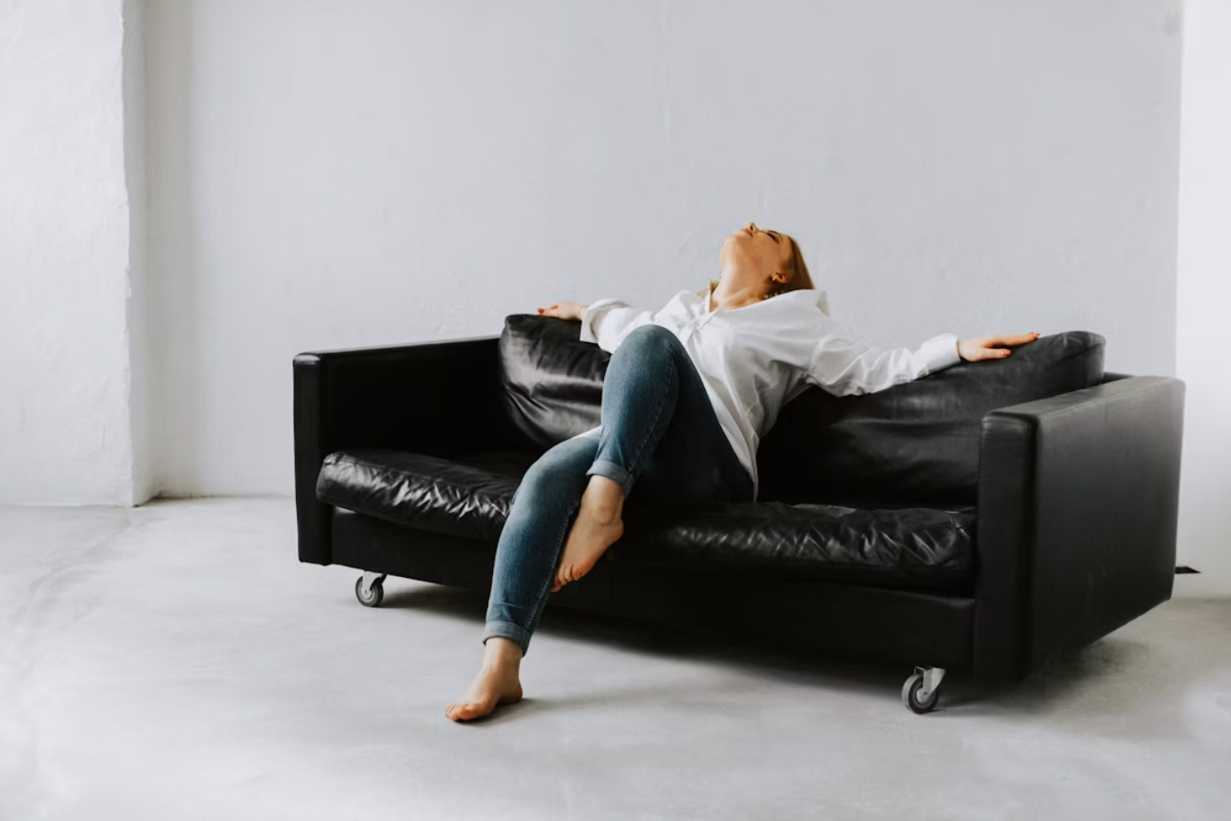 Woman sitting on black couch in white room; image by Kateryna Hliznitsova, via Unsplash.com.
