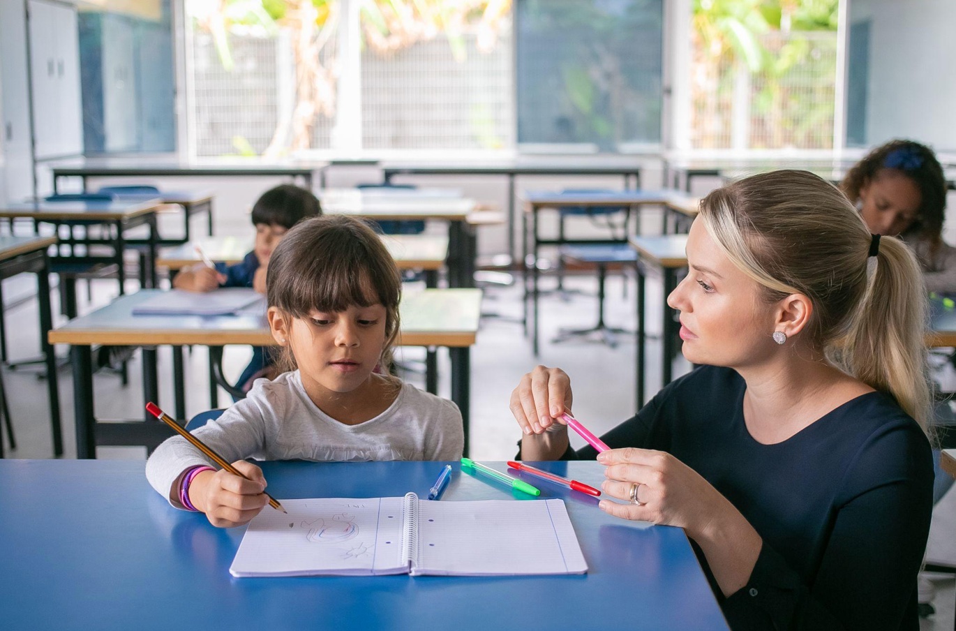 Primary school teacher helping girl with task; image by pch.vector, via Magnific.com.