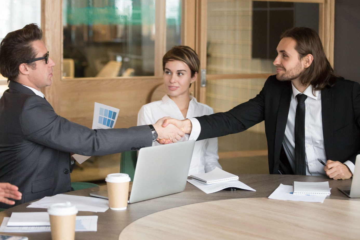 Two businessmen shaking hands while two other people look on; image by yanalya, via Magnific.com.