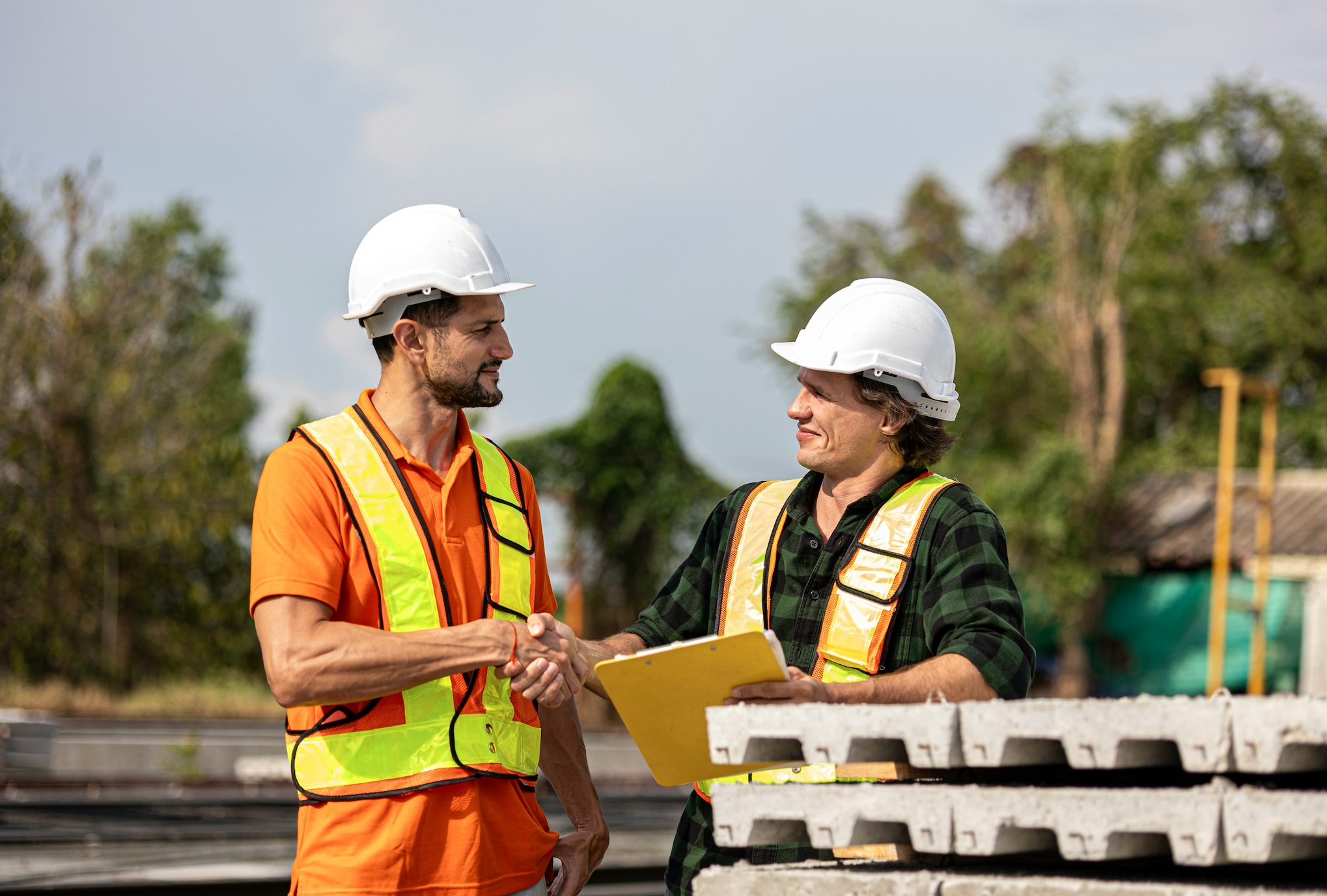 Two men in construction vests shaking hands; image by Ronnakorn Triraganon, via Unsplash.com.