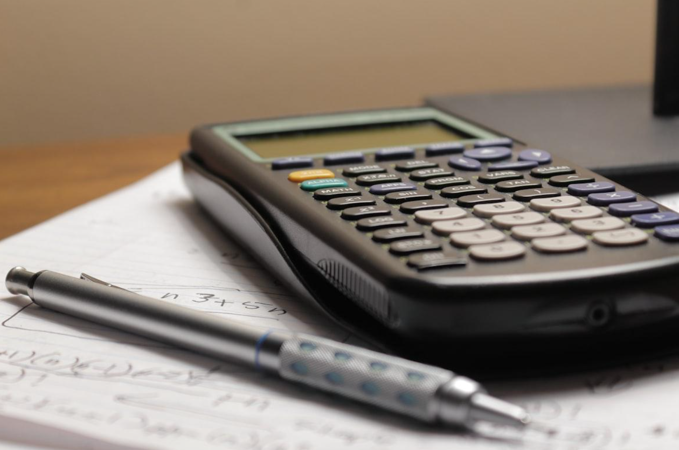 Calculator and pen sitting atop a piece of paper; image by Aaron Lefler, via Unsplash.com.